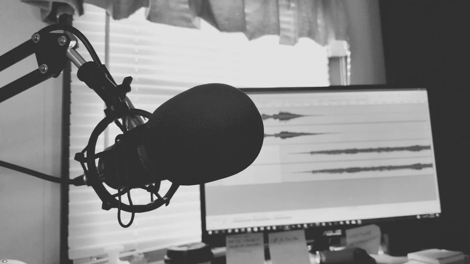 A studio microphone in front of a screen showing an audio waveform