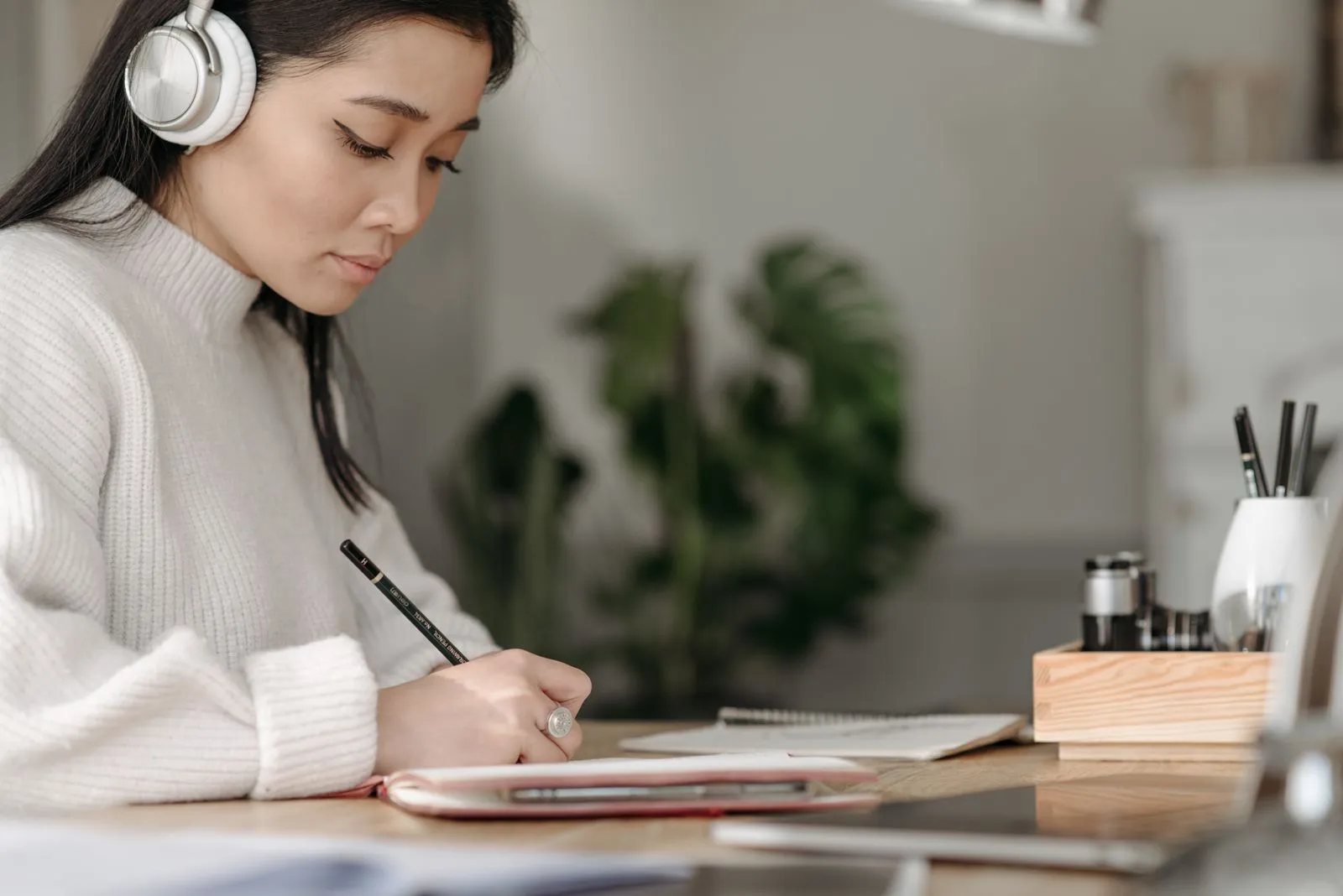 A woman wearing headphones takes notes at her desk